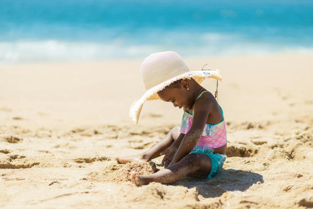 Little girl in light summer clothes playing on warm sandy beach